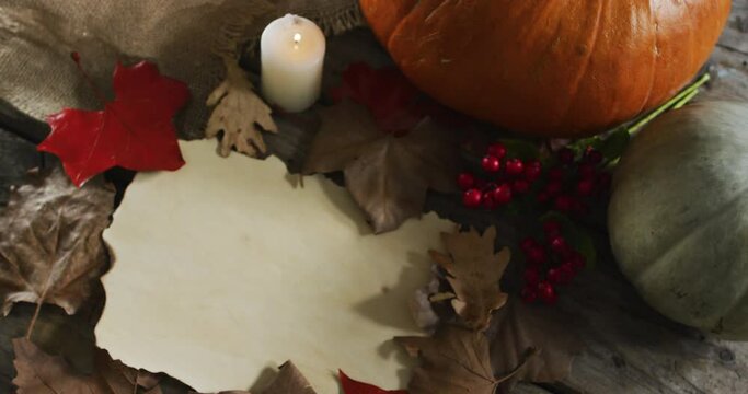 Paper with copy space against autumn leaves, candle and pumpkins on wooden surface