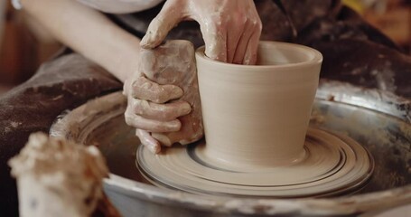 Close-up of potter's hands covered with clay making beautiful vase on throwing wheel