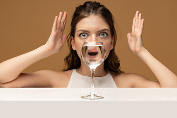 Surprise. Modern art photography. Beautiful girl's face through wine glass. Object distortion,...