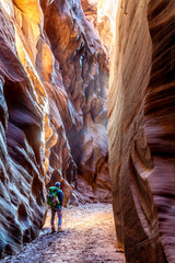 A hiker man, standing, looking at the curved walls of a slot canyon while illuminated by soft reflecting lights, Buckskin Gulch, Vermilion Cliffs Wilderness Area, Utah