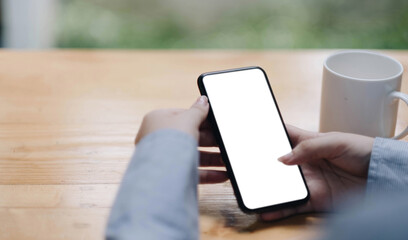 Cropped shot view of woman hands holding smart phone with blank copy space screen for your text message or information content, female reading text message on cell telephone during in urban setting.