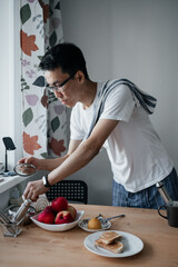 Middle aged asian man with spectacles making coffee in kitchen.