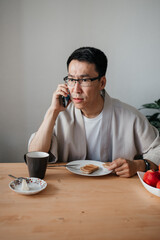 Fototapeta na wymiar Middle aged asian surprised man with spectacles talking by smartphone.
