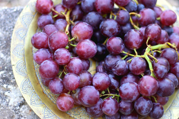 Vintage brass plate filled with fresh red grapes, served outside. Selective focus.