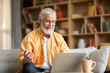 Fototapeta premium Emotional old man using laptop at home, having video call