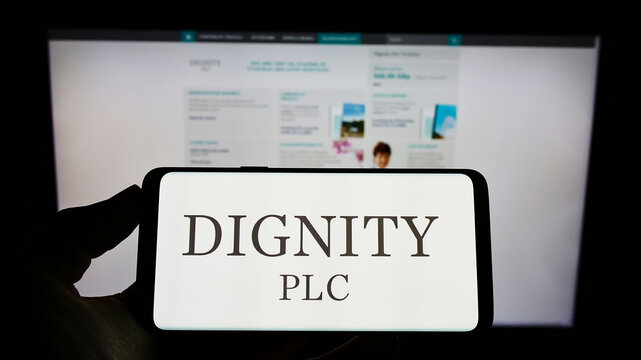 Stuttgart, Germany - 12-12-2021: Person holding cellphone with logo of funeral services company Dignity plc on screen in front of business webpage. Focus on phone display.