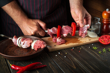 The process of cooking meat kebab in the restaurant kitchen. The chef spears raw meat on a skewer...