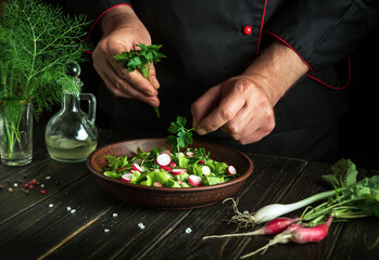 The cook prepares a fresh vegetable salad with his hands in the kitchen. Vegetarian cuisine. Hotel menu recipe