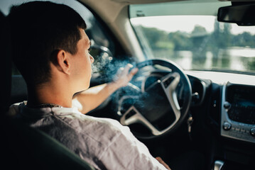 Fototapeta na wymiar Handsome Young Man smoking cigarette while Driving a Car