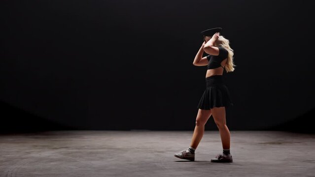 Young Woman in Policemans Hat Dances in Studio Against Black Background