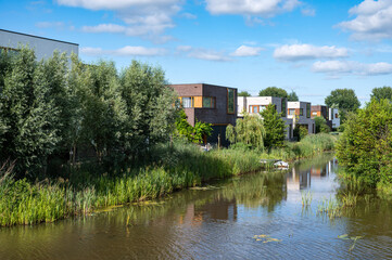 Groningen, The Netherlands, Contemporary country style houses at the waterfront surrounded by nature over blue sky in the suburbs