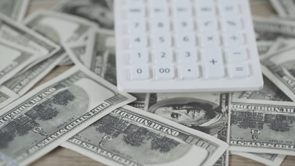 close up of white calculator on scattered dollar banknotes on wooden table