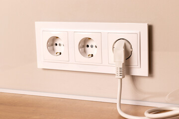 Group of white european electrical outlets with plug inserted into it on modern beige wall....