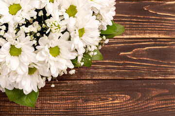 Wicker basket of white chamomile chrysanthemums on wooden background with copy space. Gift flowers basket for the holiday