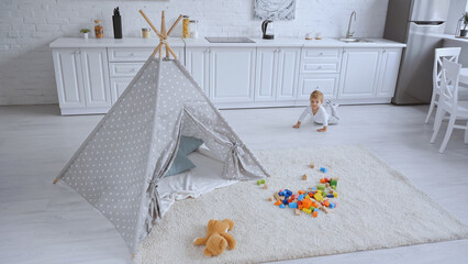 toddler boy crawling in spacious white apartment with toys and baby wigwam © LIGHTFIELD STUDIOS