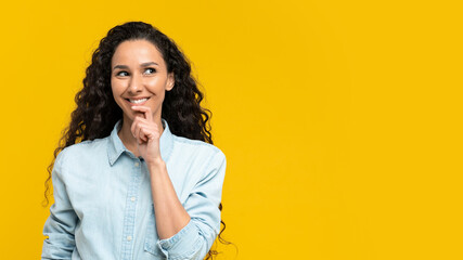Happy thoughtful young woman in casual outfit looking at empty space over yellow studio background, banner design