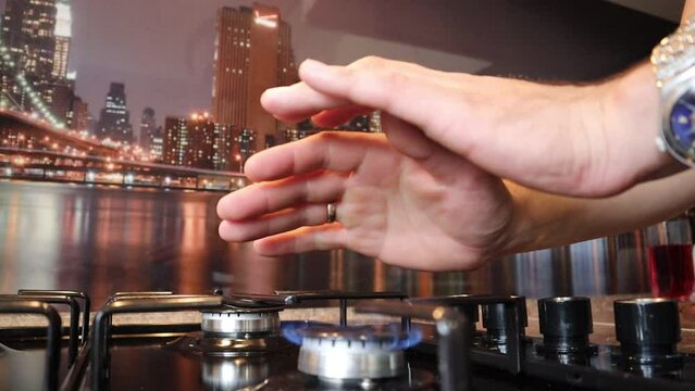 The guy rubs his frozen hands and holds them over the fire in the kitchen