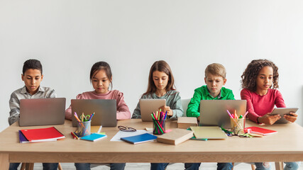 Five Multiethnic School Kids Using Laptops In Classroom, Panorama