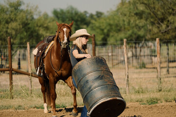 Cowgirl with barrel for rodeo practice in outdoor arena on Texas ranch.