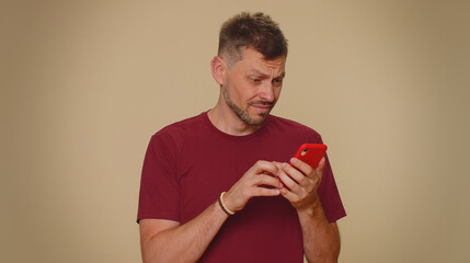 Sad young man in red t-shirt use smartphone typing browsing, loses becoming surprised sudden...