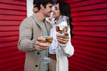 Blurred young couple kissing and holding glasses of wine near house