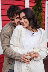 Smiling couple in cardigans holding glasses of wine outdoors