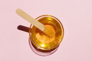 Liquid yellow sugar paste, wooden spatula on a pink background. Removing unwanted hair. Sugaring. Depilation. Epilation. Beauty. Top view. - obrazy, fototapety, plakaty