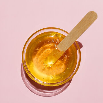 Liquid yellow sugar paste, wooden spatula on a pink background. Removing unwanted hair. Sugaring. Depilation. Epilation. Beauty. Top view.