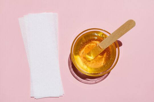 Liquid yellow sugar paste, wooden spatula, depilatory strips on a pink background. Removing unwanted hair. Sugaring. Depilation. Epilation. Beauty. Top view.
