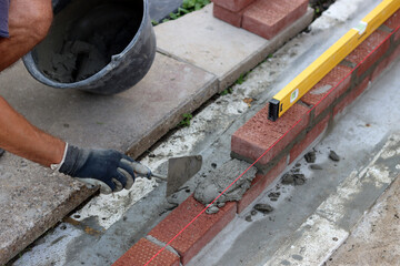 Male hands in protective gloves holding red bricks. Construction worker builds masonry.  Brickwork close up photo. 