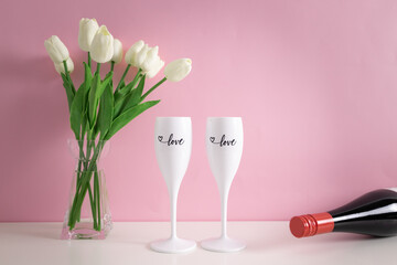 Wine bottle, two wine glasses and bouquet of white tulips on table. Set up as a surprise dinner, romantic dinner, copy space.