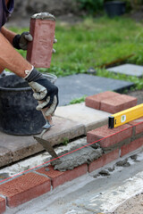 Male hands in protective gloves holding red bricks. Construction worker builds masonry.  Brickwork close up photo. 
