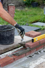 Male hands in protective gloves holding red bricks. Construction worker builds masonry.  Brickwork close up photo. 