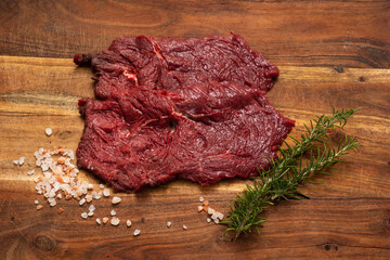 horse steaks with salt and rosemary on wooden cutting board