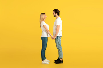 Fototapeta premium Cheerful millennial caucasian male and female in white t-shirts holding hands, looking at each other