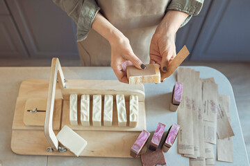 A soap maker girl holds a piece of freshly brewed handmade soap in her hands.The process of preparation and packaging.Home spa.Small business - obrazy, fototapety, plakaty
