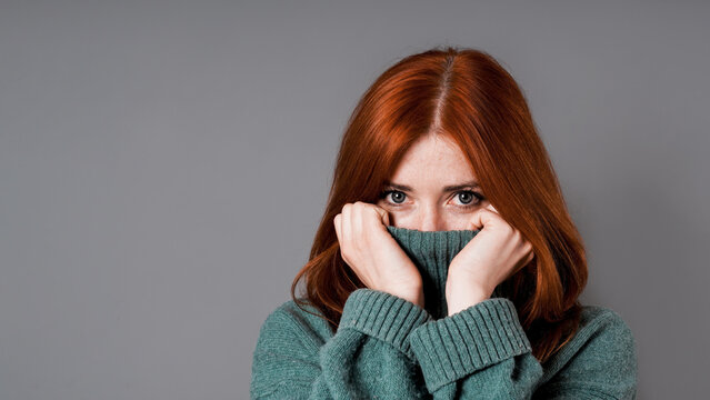 shy or embarrassed woman pulling turtleneck sweater over face