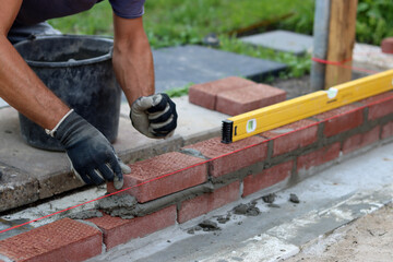 Construction work in progress. Male builder working with red bricks. Masonry wall close up photo.  