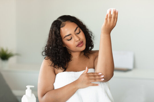 Young Black Plus Size Woman In Towel Applying Soothing Cream At Elbow, Moisturizing Dry Skin At Home, Free Space