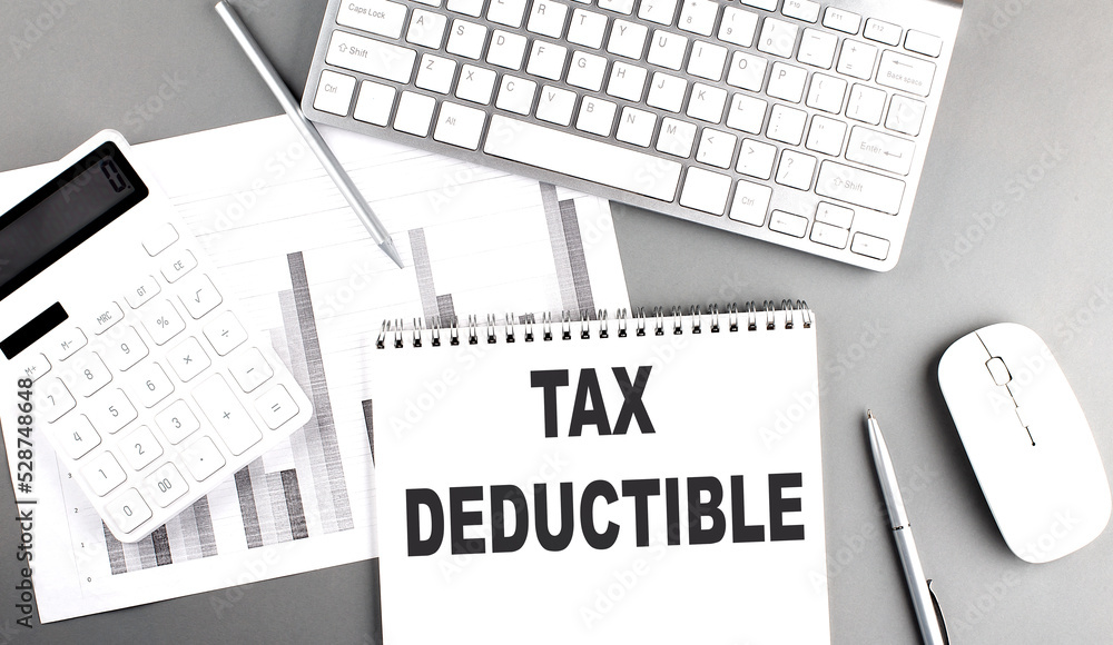 Aufkleber tax deductible text written on notebook on grey background with chart and keyboard , business concep
