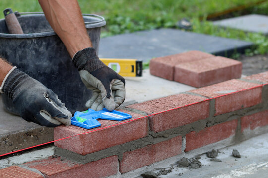 Construction work in progress. Male builder working with red bricks. Masonry wall close up photo.  