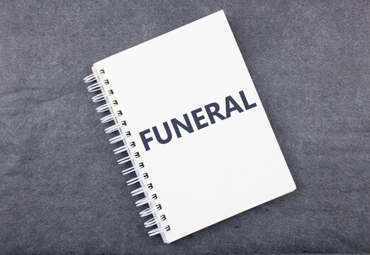 The word FUNERAL on a notebook on a black dark background. The concept of organizing a funeral.