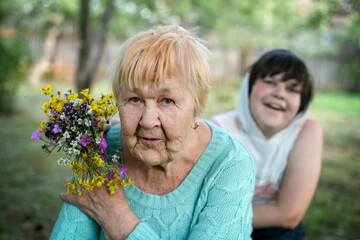 A boy grandson gives his grandmother a bouquet of wildflowers as a surprise. Grandson and grandmother spend time together. Grandmother and grandchildren enjoy spending time together in nature.