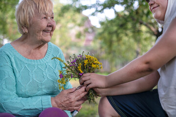 A boy grandson gives his grandmother a bouquet of wildflowers as a surprise. Grandson and grandmother spend time together. Grandmother and grandchildren enjoy spending time together in nature.