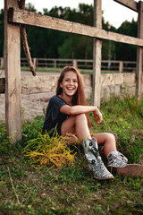 Portrait. A beautiful teenage girl in a dress and boots with long hair sits on the lawn next to the...