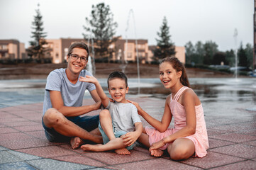 close-up of three beautiful modern children teenagers sister and two brothers sitting on a tile in...