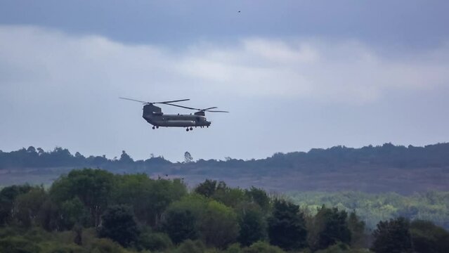 RAF Chinook tandem-rotor CH-47 helicopter flying fast and low in a cloudy blue grey sky on a military battle exercise, Wilts UK