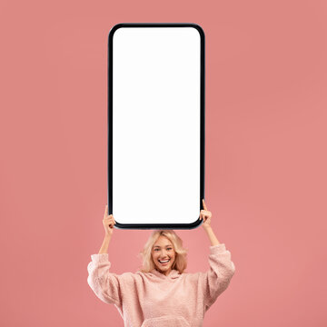 Joyful Young Blonde Woman Holding Big Blank Smartphone Above Head