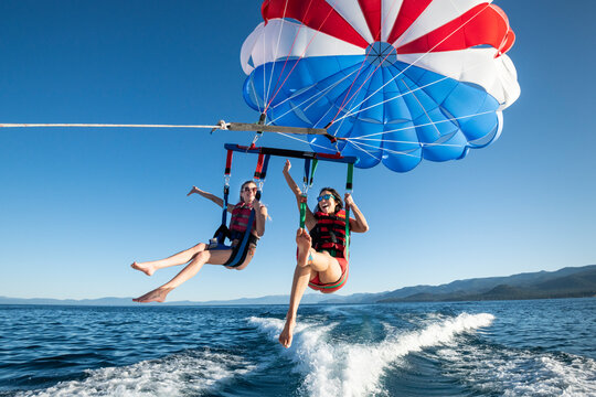 Two women smile as they enjoy a clear, Summer morning of parasailing.