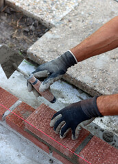 Male hands in protective gloves holding red bricks. Construction worker builds masonry.  Brickwork close up photo. 